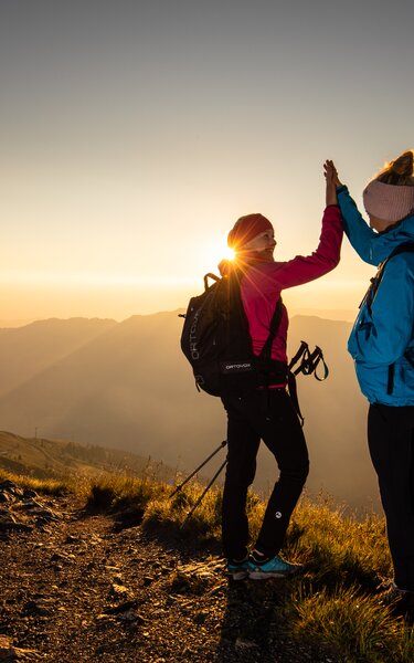 Sonnenaufgangsfahrt Wiedersberger Horn | © Alpbachtal Tourismus | shootandstyle Zwei Freundinnen klatschen vor Freude in die Hände und genießen den Sonnenaufgang am Berg | © Alpbachtal Tourismus | shootandstyle